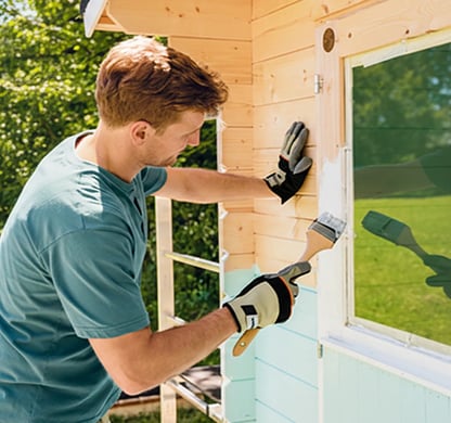Mann streicht das Holz-Gartenhaus mit einer Farbe