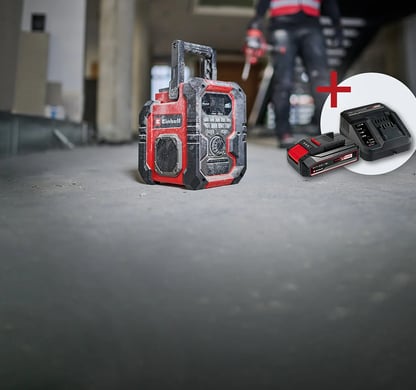 Robustes rot-schwarzes Baustellenradio auf Betonboden. Inklusive Akku und Ladegerät.
