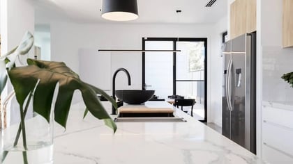 Isla de cocina moderna con grifo negro, encimera de mármol blanco y armarios de madera.