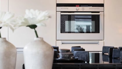 Cocina moderna con horno empotrado plateado y placa de gas negra, acentuada por flores blancas decorativas.