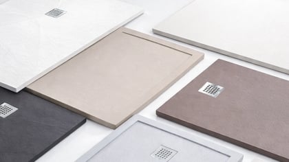 Una colección de platos de ducha texturizados en varios colores neutros, cada uno con un desagüe metálico cuadrado.