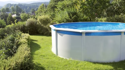 Bild eines oberirdischen Schwimmbeckens mit blauem Wasser und weißer Außenseite, umgeben von üppigem Grün.