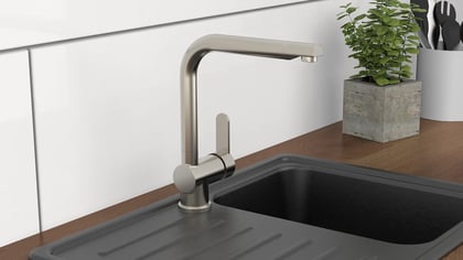 Nahaufnahme einer modernen Küchenspüle mit einem eleganten Wasserhahn, umgeben von einer Pflanze und Utensilien, die Funktionalität und Stil vereinen.