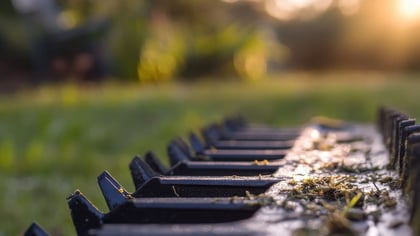 Dientes oscuros de un rastrillo con restos de hierba, de cerca en un jardín soleado.