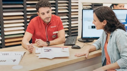 Consulta de diseño de muebles, con cliente y asistente revisando muestras de materiales y planos 3D.