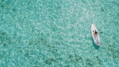 Paddelboard-Abenteuer: Eine Person genießt das Stand-Up-Paddling auf türkisfarbenem Wasser.