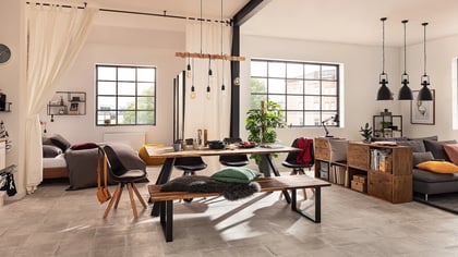 Einladender Wohnraum mit einem Holztisch, einer Bank mit Fellauflage und einem grauen Sofa. Moderne Einrichtung in einem Loft-artigen Ambiente.