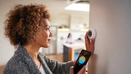 Eine Frau bedient ein smartes Thermostat mit ihrem Handy, um die Temperatur zu regulieren.