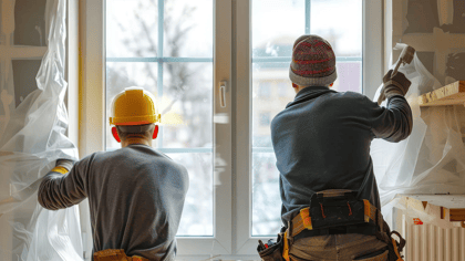 Zwei Bauarbeiter installieren oder bereiten Fenster in einem renovierten Raum vor, von hinten gesehen.