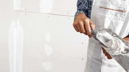 Handwerker trägt Spachtelmasse mit einer Glättekelle auf Trockenbau auf.