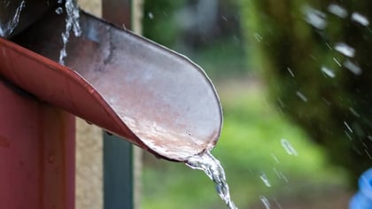 Extensión de bajante roja dirigiendo el agua de lluvia a un barril de recolección azul.