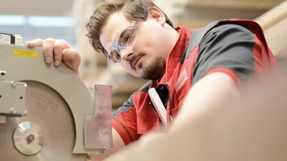 Nahaufnahme eines Mannes mit Schutzbrille, der an einer industriellen Schleifmaschine arbeitet, wobei der Fokus auf der Maschine liegt.