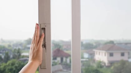 Mano operando una manilla de ventana corredera con vista exterior.