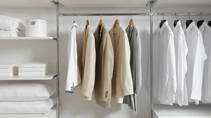 Gepflegter Kleiderschrank mit weissen Hemden, beigen Jacken und gestapelten Handtüchern. Ordnung im Schrank für ein stilvolles Zuhause.