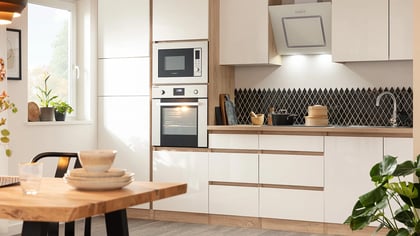 Essbereich mit Holztisch, Geschirr und Küchenbereich mit Einbaugeräten und Kochutensilien. Helle und moderne Einrichtung.
