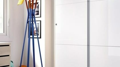 Habitación moderna con un armario blanco brillante de puertas correderas y un escritorio de madera clara con cajones.