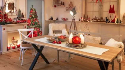 Ein festlich dekoriertes Zimmer für Weihnachten mit Esstisch, beleuchtetem Baum, roten/weißen Ornamenten und saisonalen Figuren.