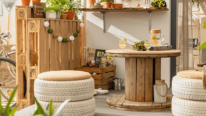 Ein gemütlicher Außenbereich mit einem Tisch aus einer Kabeltrommel und Sitzgelegenheiten aus recycelten Reifen, dekoriert mit Pflanzen und Lichtern.