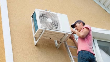 Un técnico instala una unidad exterior de aire acondicionado blanca en la pared de un edificio.