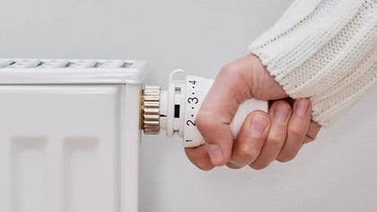 Mano con suéter blanco ajustando el termostato del radiador blanco.