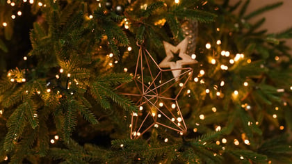 Geometrischer kupferfarbener Metallsternschmuck an einem Weihnachtsbaum mit warmen Lichterketten.