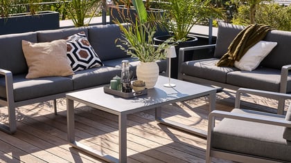 Conjunto de salón exterior moderno con marco de metal gris y cojines gris oscuro sobre una cubierta de madera, para relajarse.