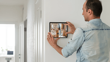 Ein Mann hält ein Tablet an der Wand, das Überwachungsaufnahmen des Hauses zeigt. Es zeigt Sicherheit und Kontrolle.
