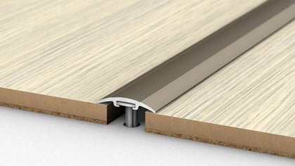 Silberne gerippte Bodenübergangsleiste aus Metall, die zwei helle Holzoptik-Bodenplatten mit Korkunterlage verbindet.