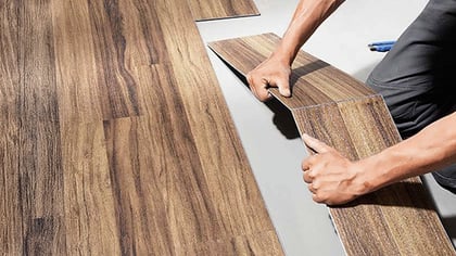 Braune Holzoptik-Bodenplatten werden von einer Person verlegt, das Klick-System ist sichtbar.