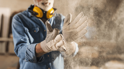 Ein Mann schüttelt Handschuhe, Staubwolke entsteht. Arbeitshandschuhe bieten Schutz und Griffigkeit bei handwerklichen Tätigkeiten in der Werkstatt.