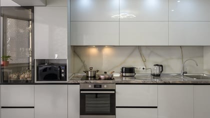 Cocina moderna con elegantes armarios gris claro, encimeras de mármol y electrodomésticos integrados, incluido microondas y horno.