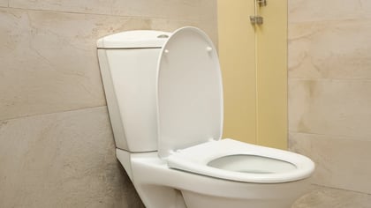 Nahaufnahme einer weißen Toilette mit offenem Deckel in einem Badezimmer mit beigen Fliesen.
