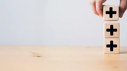 Ein Handschuh mit rotem Handrücken und schwarzer Handfläche trifft auf eine Hand mit erhobenem Daumen vor grauem Hintergrund.