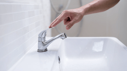 Einarmiger Wasserhahn aus Chrom in einem modernen Badezimmer. Der Wasserhahn wird von einer Hand bedient, um das Wasser ein- oder auszuschalten.
