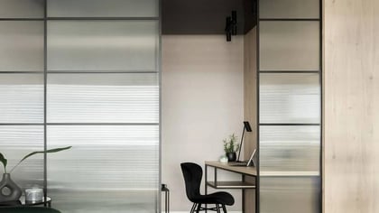 Divisor de ambientes moderno con paneles de vidrio esmerilado y marcos negros, con escritorio de madera clara integrado para oficina.