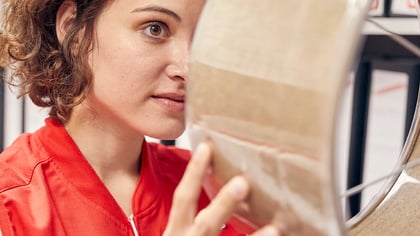 Una mujer con chaqueta roja examina un documento marrón claro dentro de una funda protectora transparente.