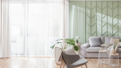 Einladender Wohnraum mit grauer Couch, Akzentwand und natürlichem Licht. Die weißen Vorhänge sorgen für eine helle, freundliche Atmosphäre.