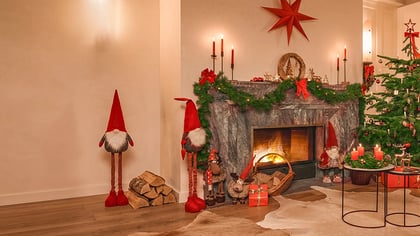 Ein gemütliches Wohnzimmer, weihnachtlich geschmückt mit Kamin, beleuchtetem Baum und festlichen Wichteln.