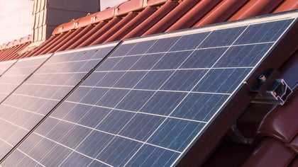 Primer plano de paneles solares en un tejado de tejas rojas, que generan energía renovable y reducen las facturas de electricidad.