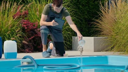 Técnico añadiendo productos químicos a una piscina, con equipo de prueba y grandes contenedores.