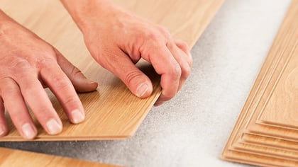 Manos instalando tablas de suelo laminado de aspecto de madera clara, encajándolas.
