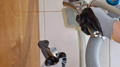 Manos enguantadas usando una llave inglesa ajustable para apretar una conexión de fontanería.