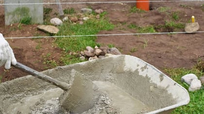 Mano enguantada mezclando hormigón húmedo en una carretilla con una pala para construcción.