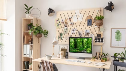 Ein moderner Arbeitsbereich mit einem großen Monitor, Pflanzen und einer hölzernen Pinnwand, der eine ruhige, natürliche Atmosphäre schafft.\n