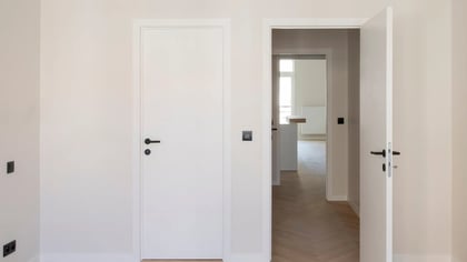 Puertas interiores modernas en blanco con manijas negras en una habitación luminosa. El suelo tiene un patrón de parqué.
