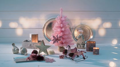 Festliche rosa und silberne Weihnachtsdekorationen: Baum, Schneemann, Schaukelpferde und Kerzenhalter auf Holz.