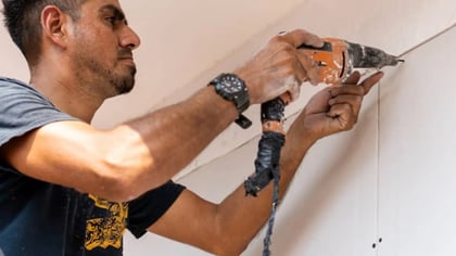 Hombre usa un taladro naranja y negro para taladrar una pared clara.