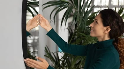 Mujer interactuando con un espejo inteligente o pantalla grande, tocando su reflejo.