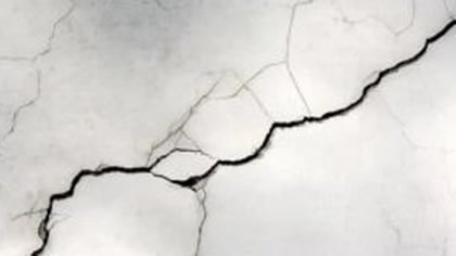 Superficie gris claro agrietada con prominentes grietas oscuras e irregulares.
