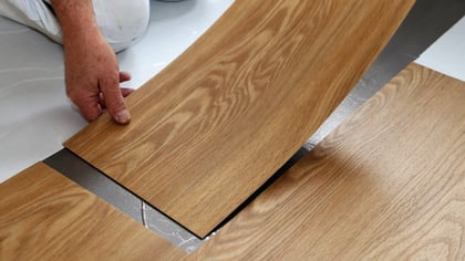 Manos instalando lamas de suelo efecto roble claro. Las lamas presentan una textura de veta de madera realista, ideal para una renovación sencilla.